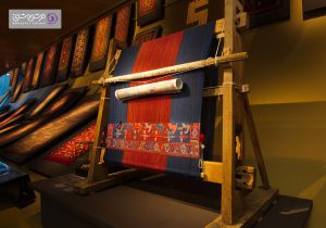 تصویری از دار قالی در فضای داخلی موزه قرار گرفته است.