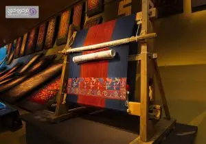 تصویری از دار قالی در فضای داخلی موزه قرار گرفته است.